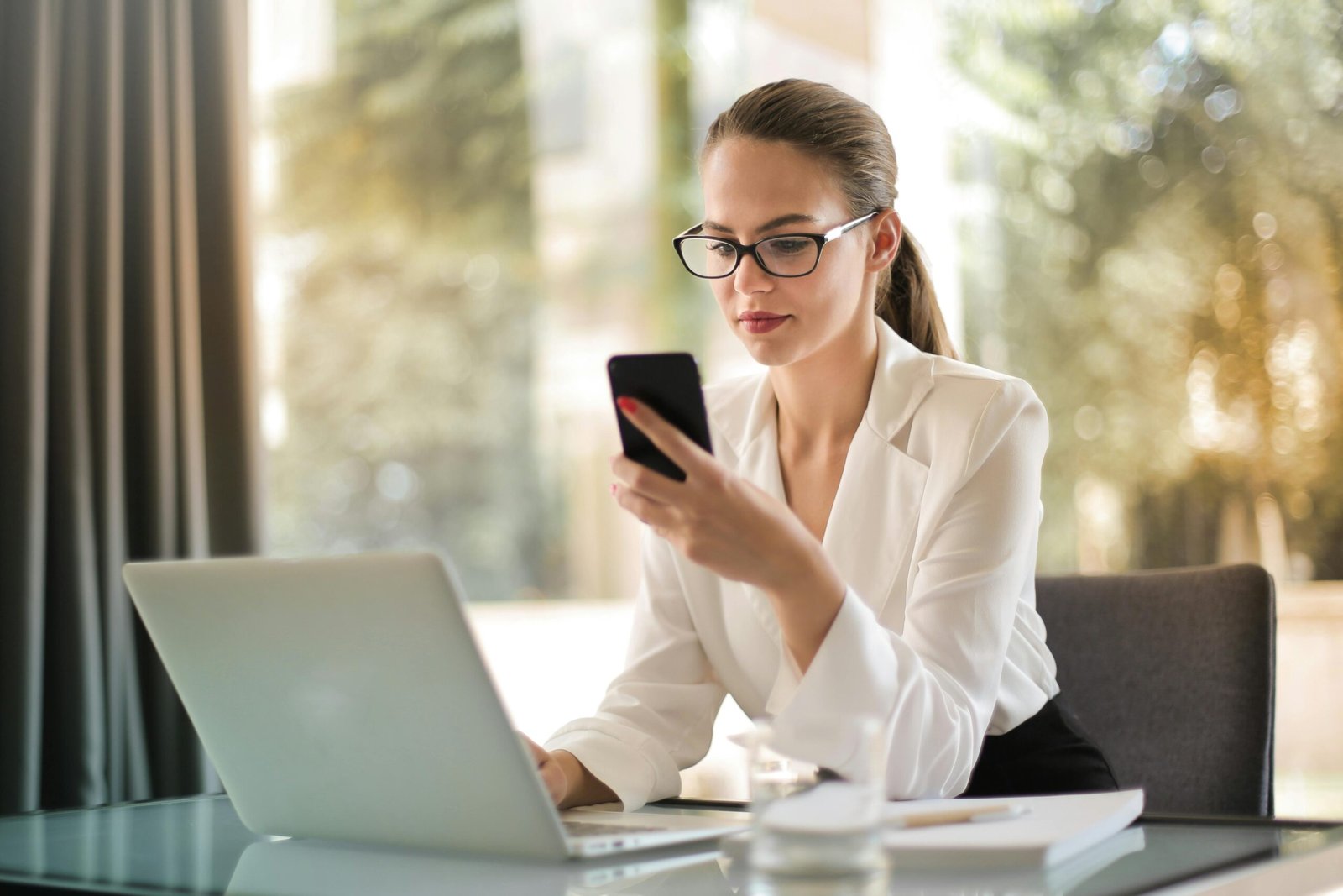 Businesswoman using smartphone and laptop at office desk